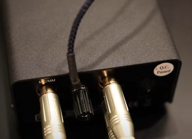 Close-up of an audio device with MC/MM inputs and connected gold-plated RCA cables.